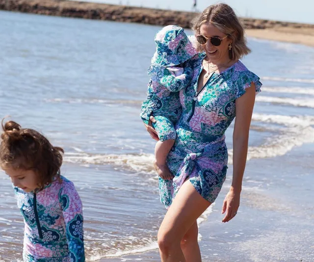 Woman and two children in matching floral outfits walk by the beach.