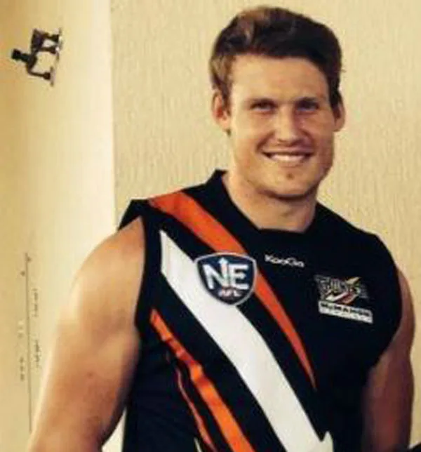 Man in black sports jersey with orange and white stripes, smiling at the camera.