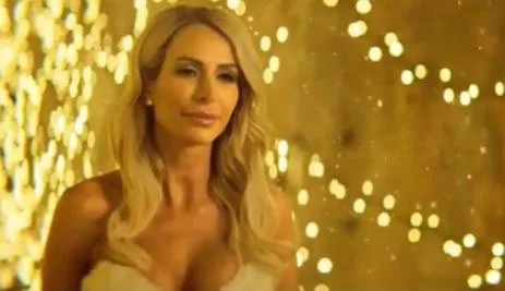 Blonde woman in a strapless dress stands in front of golden fairy lights, creating a warm, glowing background.