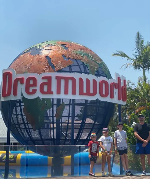 Group of people posing in front of the Dreamworld globe sign with clear skies and palm trees in the background.