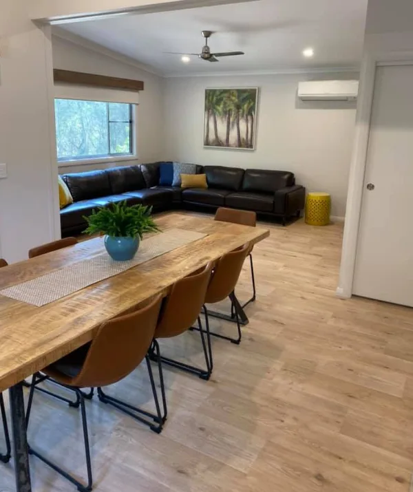 "Modern living room with wooden dining table, brown chairs, black sectional sofa, art, and potted plant."