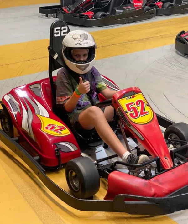 A person in a helmet gives a thumbs-up while sitting in a red go-kart numbered 52 on a track.