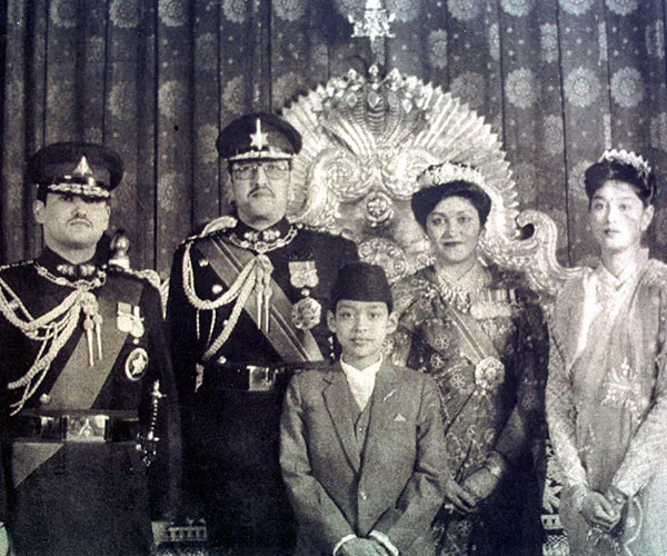 A historical photo of a royal family with three men in military uniforms and two women in traditional attire standing indoors.