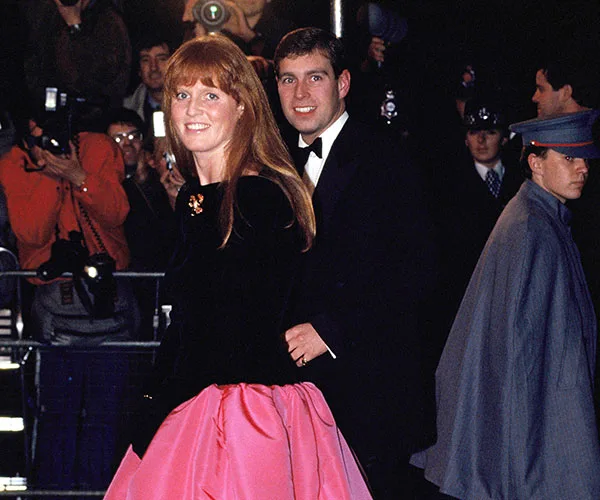 Two people in formal attire at a public event, with photographers in the background.