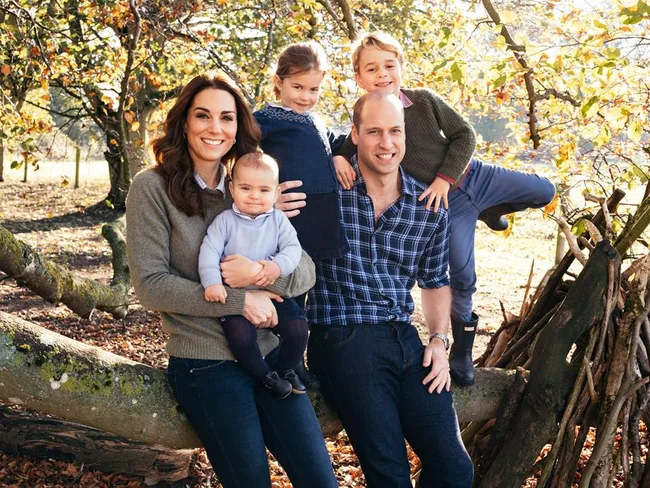 Family sitting outdoors on a log in an autumnal setting, smiling for the camera.