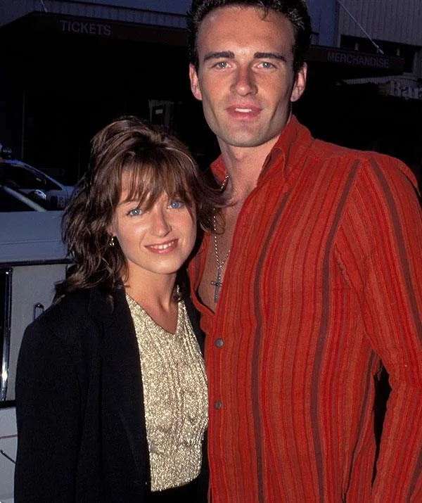 Two individuals posing together, one in a striped shirt, the other in a gold top and black jacket, smiling at the camera.