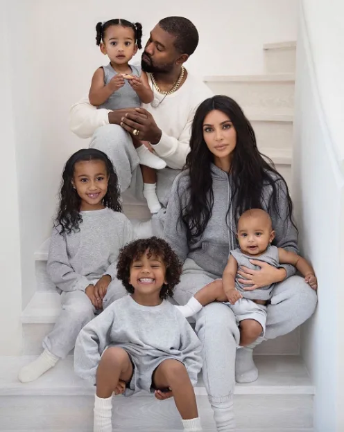 A family of six sits on stairs, all wearing matching gray outfits, with parents holding two of the children.