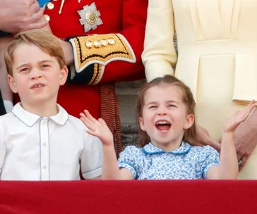 Children smiling and raising hands at a public event, with adults standing behind them.