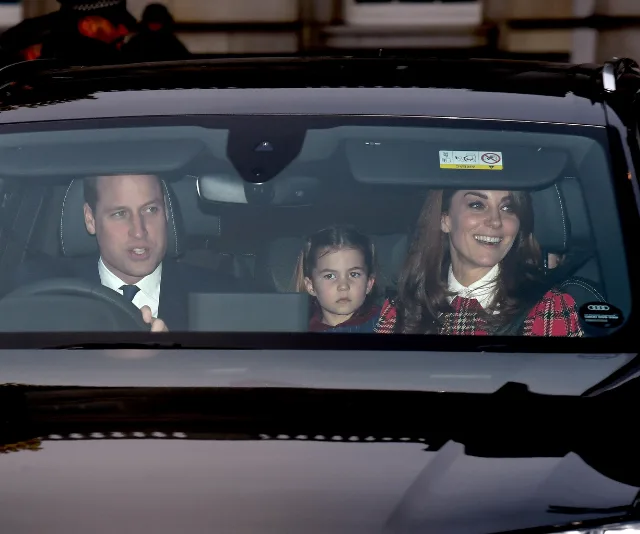 A family in a car, with a man driving, a woman smiling, and a child seated between them, looking straight ahead.