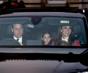 A family in a car, with a man driving, a woman smiling, and a child seated between them, looking straight ahead.