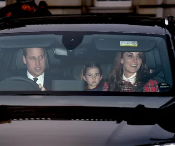 A family in a car, with a man driving, a woman smiling, and a child seated between them, looking straight ahead.