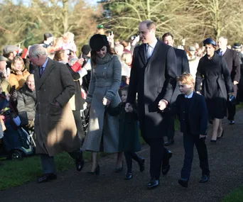 Royal family walking outdoors on Christmas, surrounded by crowds dressed warmly, children holding hands with adults.