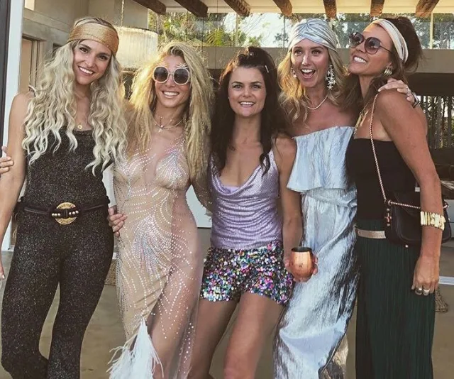 Group of women in glamorous, festive outfits posing together at a party.