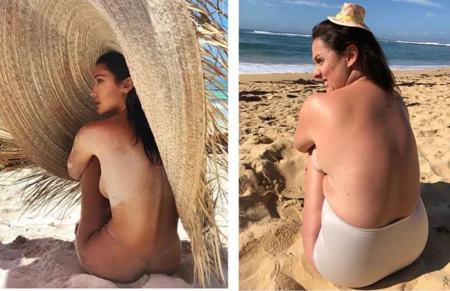 Two women on a beach; left in a large hat, right in a small hat, both sitting on the sand facing away.