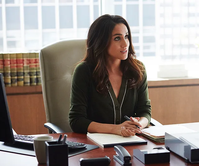 A woman in a green cardigan sits at an office desk with a notepad, surrounded by legal books and a computer.