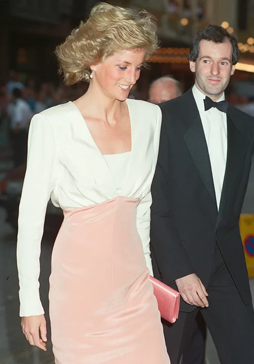 A woman in a white and pink dress walking beside a man in a tuxedo at an event.