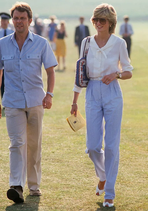 Man in light shirt and pants walking with a woman in a white blouse and striped pants, carrying a bag and document.