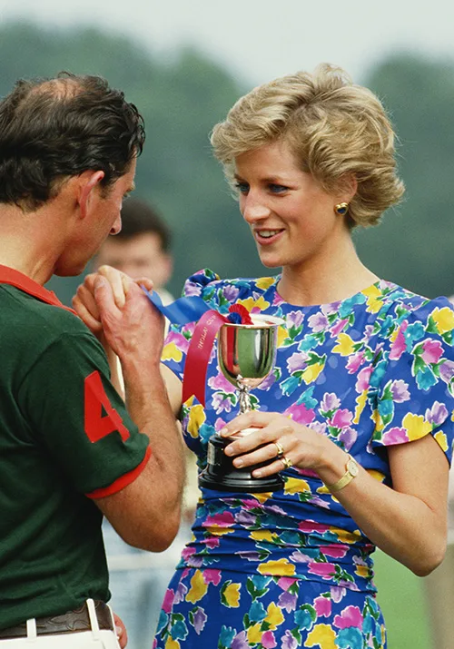 Prince Charles receives a trophy from Princess Diana, smiling, wearing a floral dress, during a polo match.