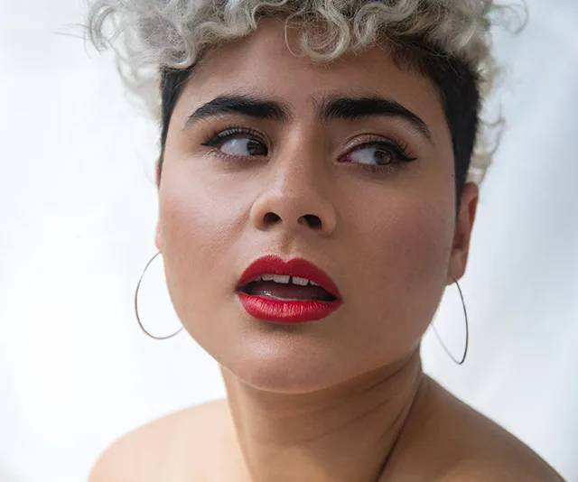 Person with curly hair and hoop earrings looking to the side, wearing bright red lipstick.