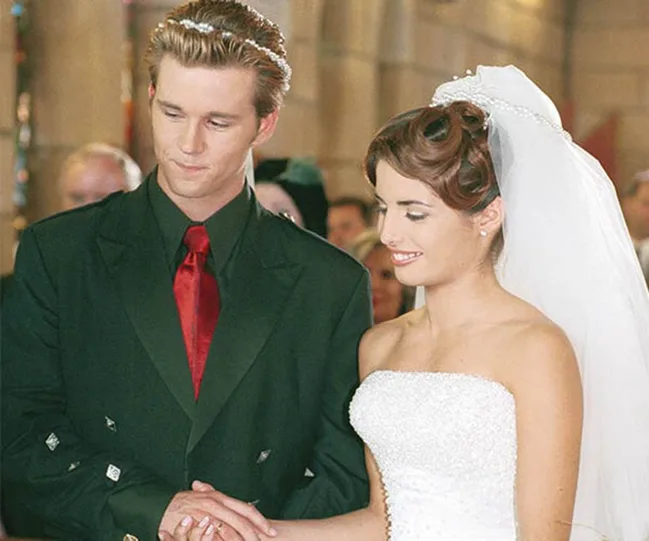 A couple holding hands, standing at the altar in wedding attire; the bride in a white dress and the groom in a dark suit.