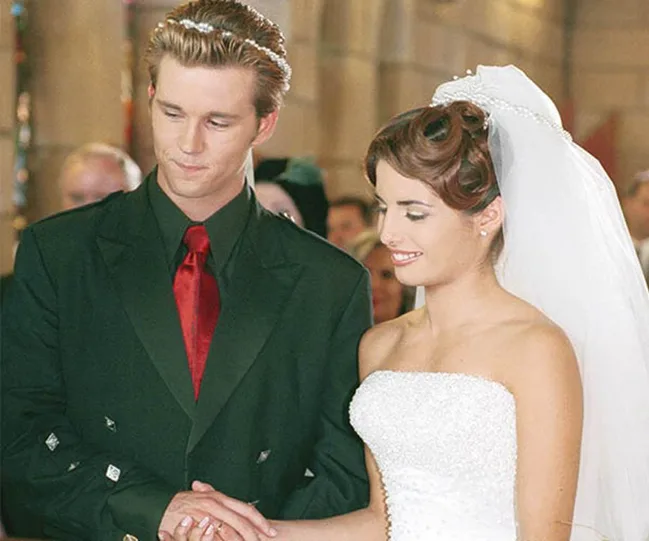 A couple holding hands, standing at the altar in wedding attire; the bride in a white dress and the groom in a dark suit.