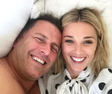 A smiling couple lying in bed, close together, with polka dot fabric visible.