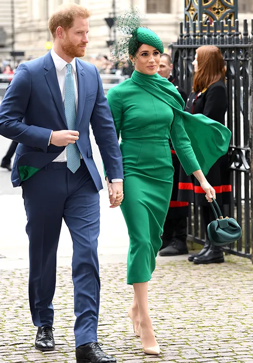 A couple walking hand-in-hand, with the woman in a green outfit and hat, and the man in a blue suit with a tie.