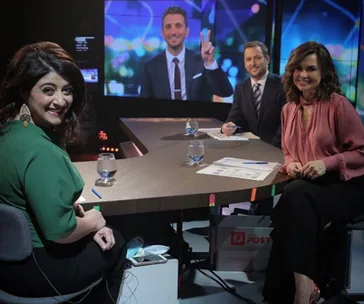 Group of TV show hosts in studio, smiling at the camera with a video call screen in the background.