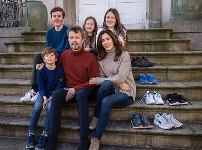 Family of five sitting on outdoor steps with running shoes placed beside them.