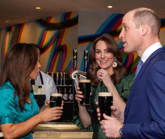 Three people holding pints in a colorful bar setting, two women in blue and green, one man in a suit.