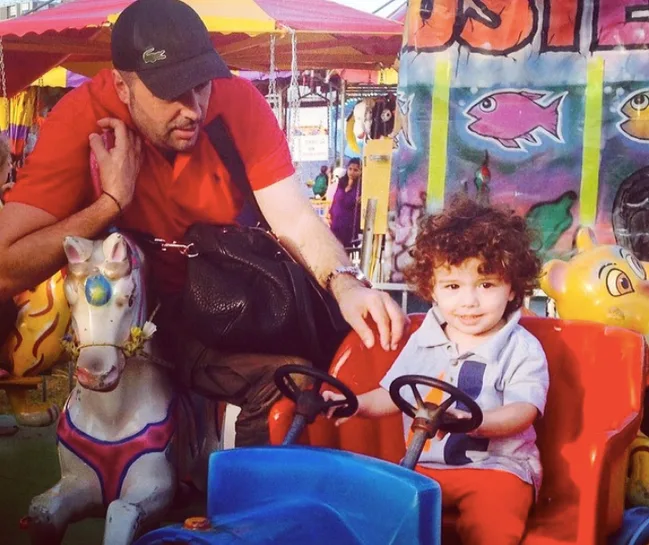 Man with a cap helping a child on a carnival ride with colorful background.