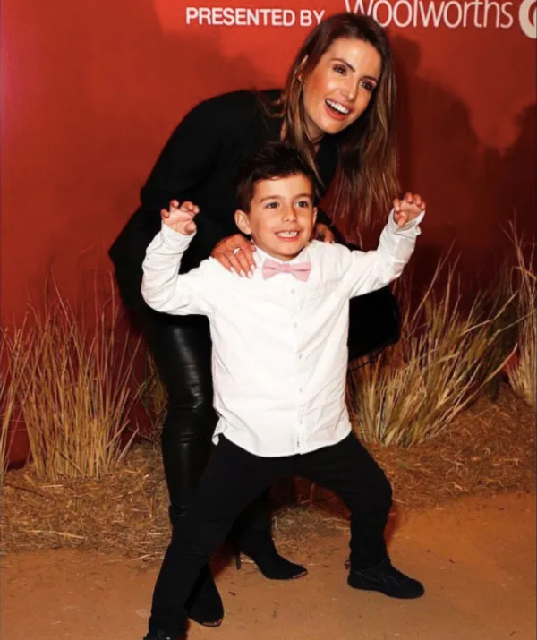 Woman in black and boy in white shirt and pink bow tie pose playfully on a red carpet event.
