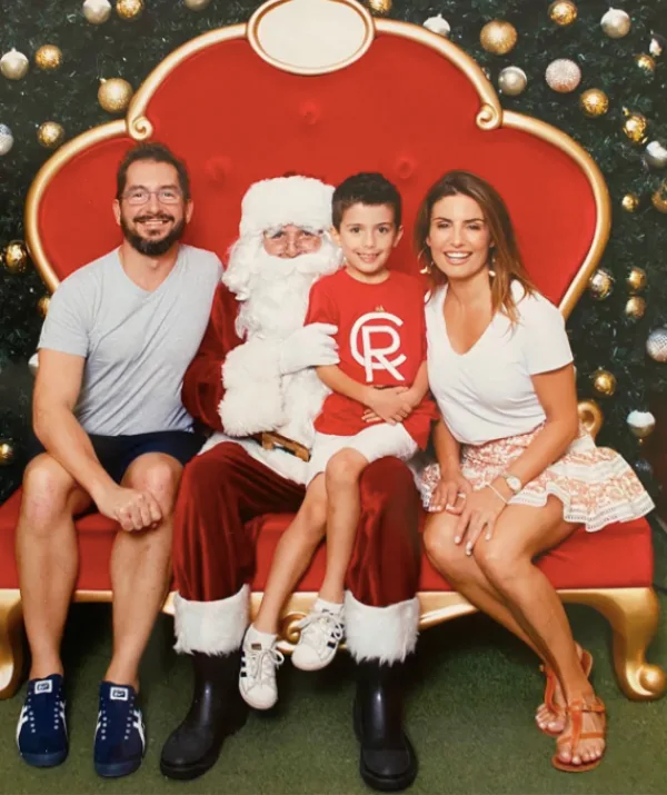 Family sitting with Santa Claus on a red chair, surrounded by a festive holiday background.