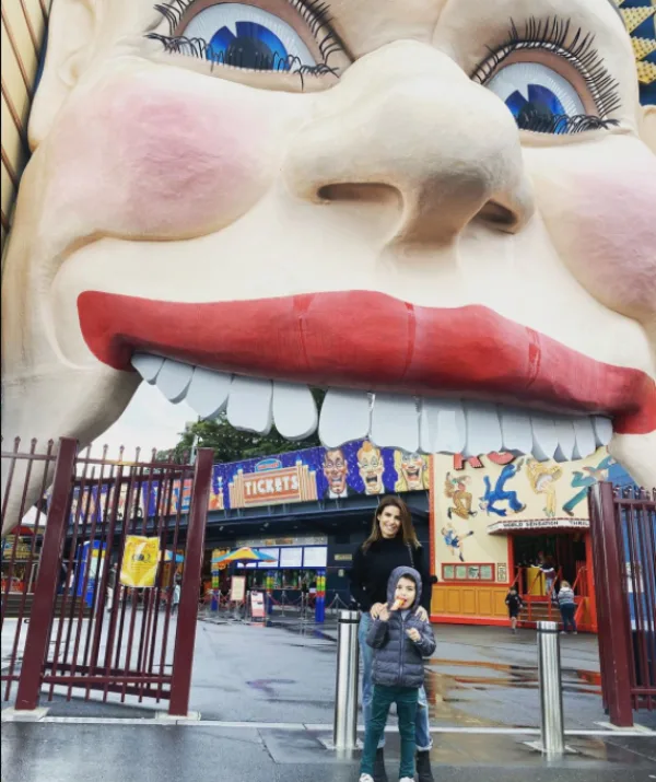 A large clown face entrance at Luna Park, with a woman and child standing underneath on a rainy day.