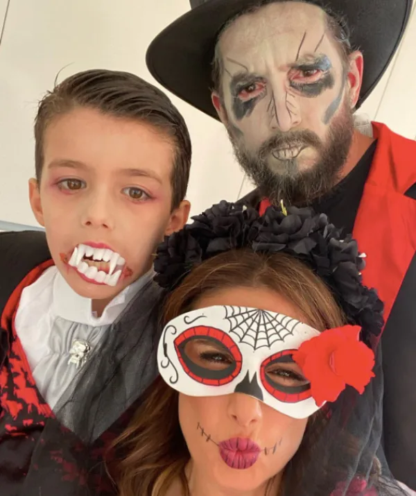Family in Halloween costumes: vampire boy, Catrina woman with mask, and man with skeleton face paint and hat.