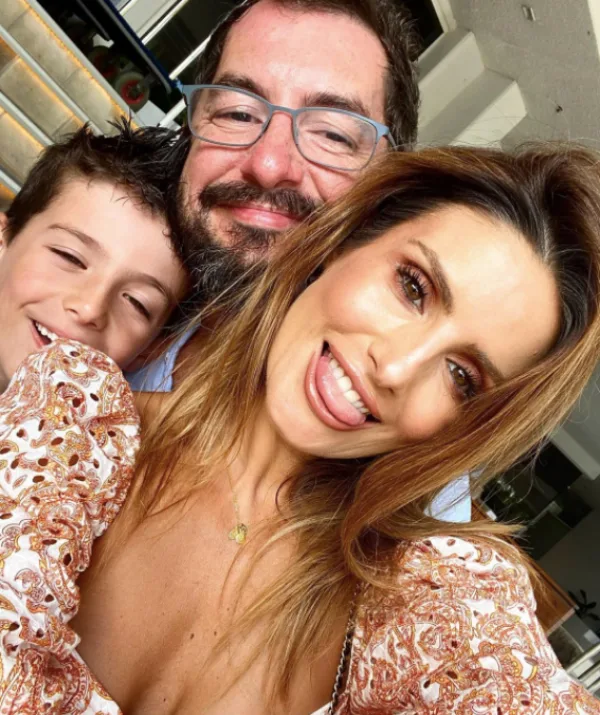 Family selfie with a woman smiling and posing playfully, a man behind her, and a young boy on the left.
