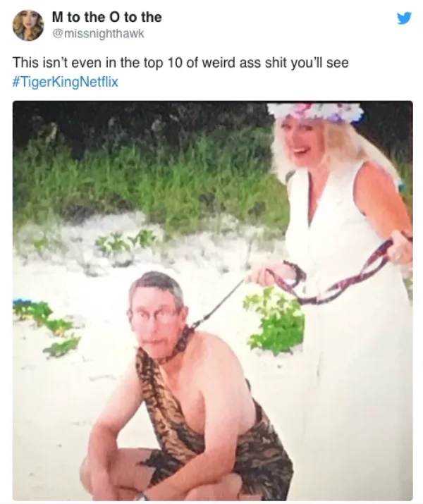 Man in tiger print outfit on leash held by laughing woman in white dress, on a sandy beach. #TigerKingNetflix.
