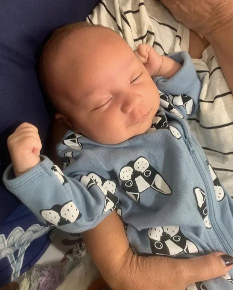 Baby in a blue onesie with panda designs, sleeping peacefully in someone's arms.
