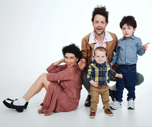 Family of four posing in a studio; a woman sitting, a man kneeling, and two young children standing near them.