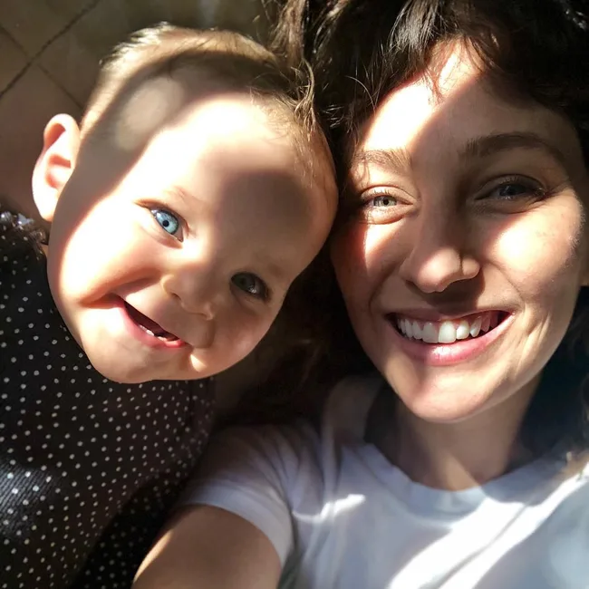 Mother and baby smiling in sunlight shadows, close-up selfie.