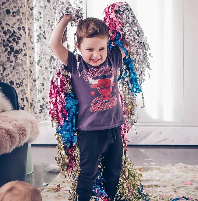 Child in a Chicago Bulls shirt playing with colorful streamers, smiling joyfully in a room.