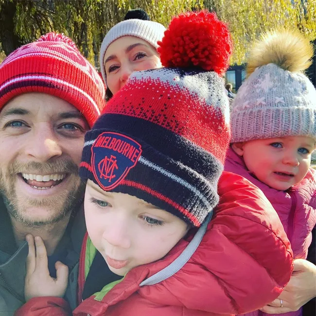 Family selfie outdoors in winter attire; adults and two children wearing knitted hats.