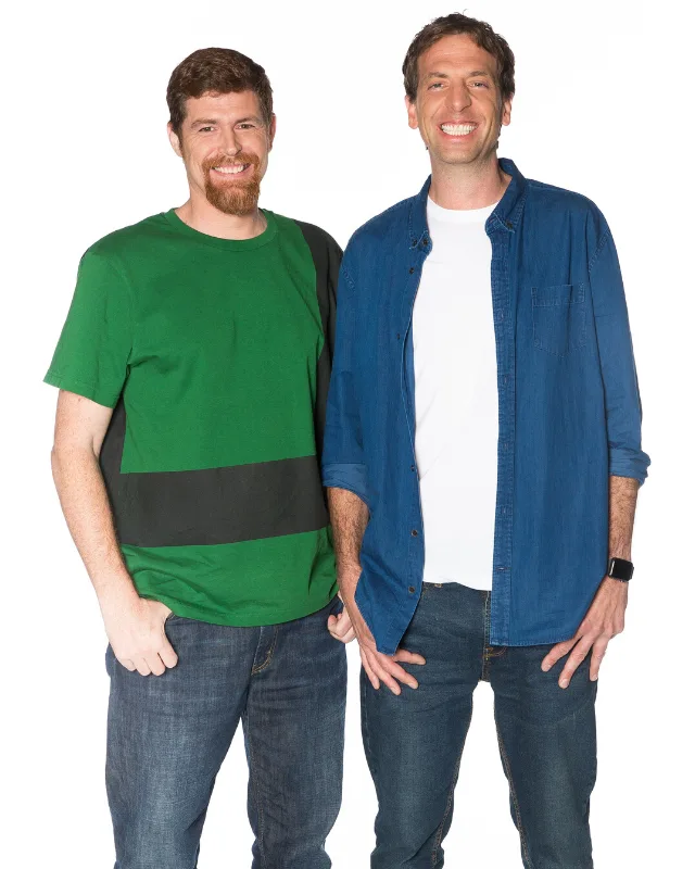 Two smiling men standing side by side; one in a green shirt, the other in a blue shirt, both wearing jeans.