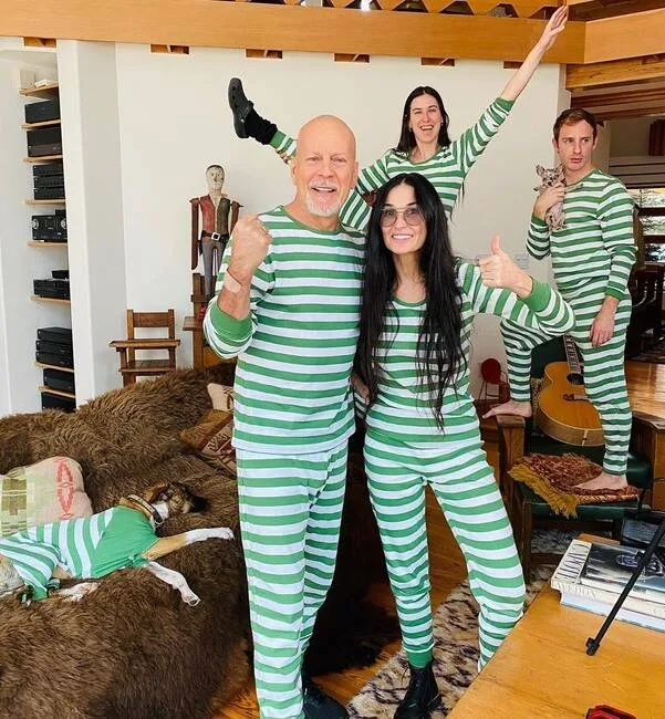 Four people and a dog, all in matching green and white striped outfits, in a cozy room with books and a guitar.