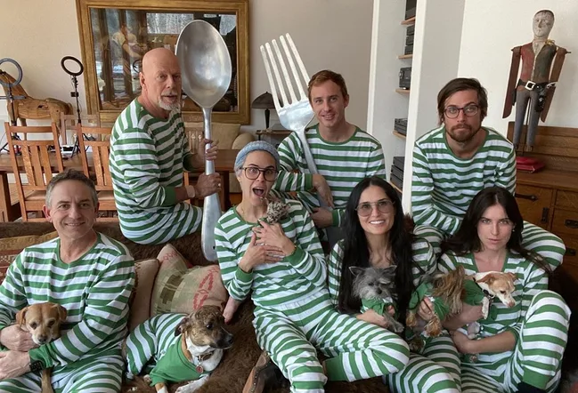 Family in matching green striped pajamas, holding large spoon and fork, with dogs on a couch.