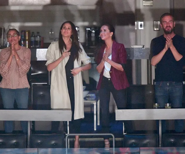 Four people stand clapping in a dimly lit room.
