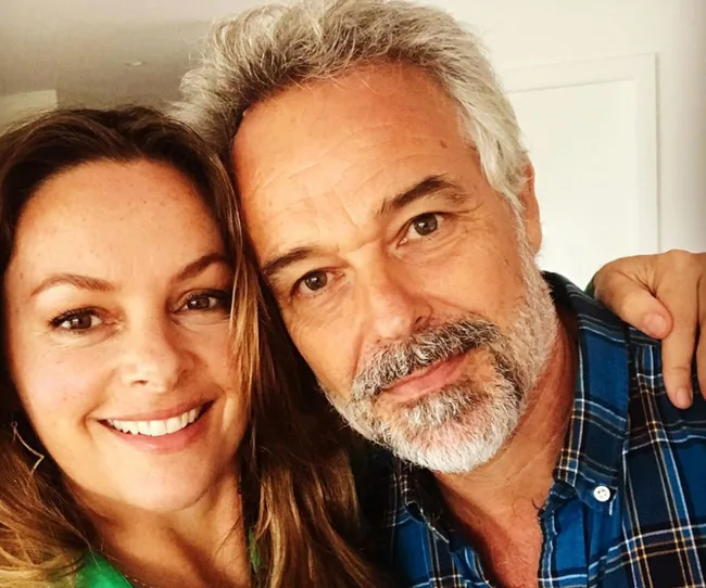 A smiling man and woman in a close embrace, both wearing casual attire.