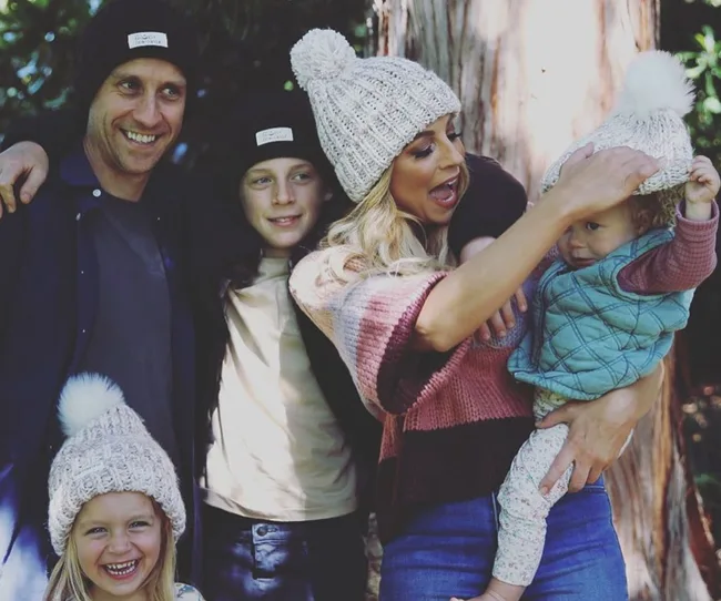 Family of five in cozy hats smiling in a forest setting.
