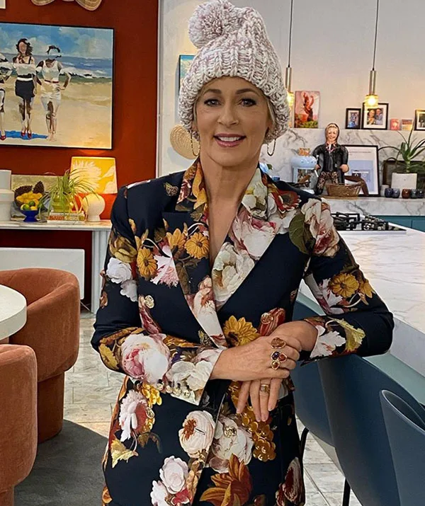 Woman in a floral suit and knit hat standing in a decorated kitchen, smiling at the camera.
