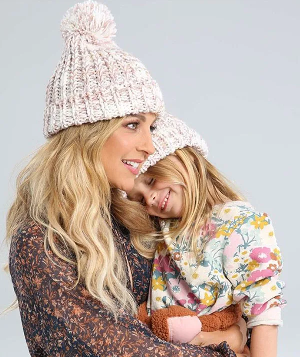 A woman and a young girl wearing knit hats smile and hug each other affectionately.